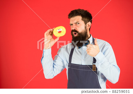 Hipster bearded baker hold glazed donut on red background. Cafe and bakery concept. Sweet donut from baker. Man bearded baker in apron hold cute dessert. Private bakery business. Just try this 88259031