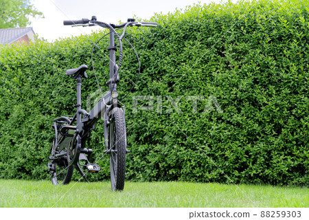 Black e bicycle against green hedge 88259303