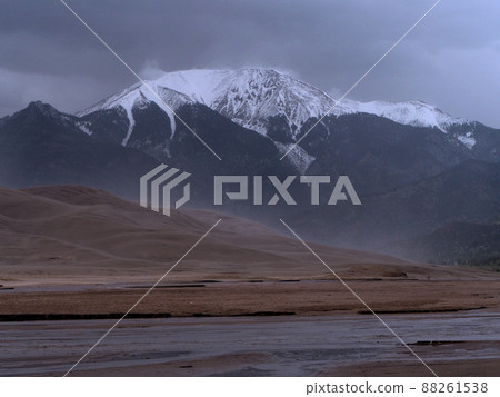 The cordillera mountain range with white peaks towering over the large sand dunes and their background 88261538