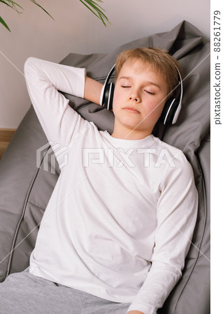 Relaxed teenager lies on a bean bag chair with headphones. White t-shirt mockup 88261779