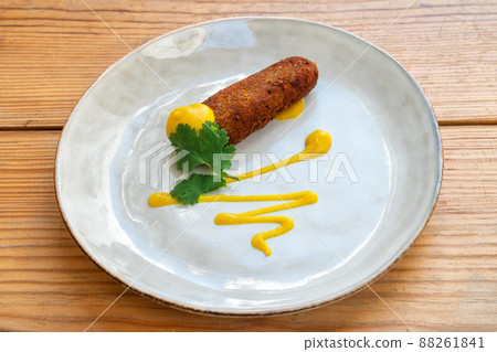 Fried croquette appetizer drizzled with mustard sauce, mediterranean appetizer. On a plate on a wooden background close-up. 88261841