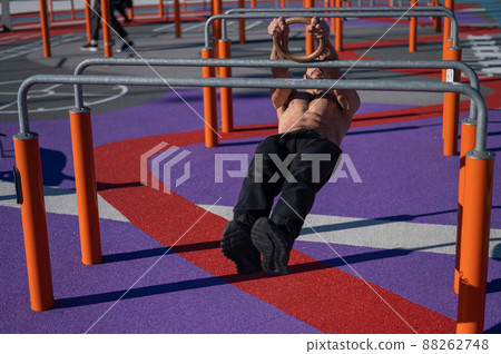 Shirtless man doing horizontal balance on parallel bars at sports ground.  88262748