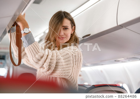 Woman putting bag in overhead luggage bin in airplane 88264486