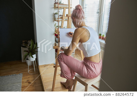 Lady artist in casual clothes at work upon picture on blank canvas at home Lady artist in casual clothes at work upon picture on blank canvas at home 88264572