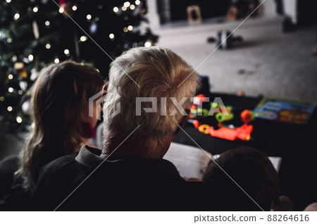 Grandpa reading a storybook to two grandkids sitting on his lap 88264616