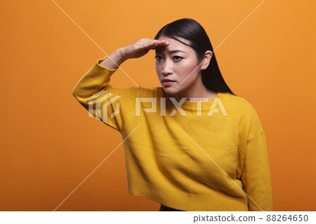 Curious intrigued asian woman holding hand above eyes and peering into distance. Young adult person with palm on forehead looking far away and searching for someone on horizon, Curious intrigued asian woman holding hand above eyes and peering into distance. Young adult person with palm on forehead looking far away and searching for someone on horizon, 88264650