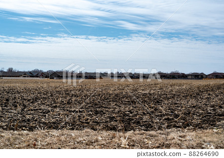 Empty corn field after fall harvest with residue over soil. Urban sprawl visible in the distance with residential housing development. Empty corn field after fall harvest with residue over soil. Urban sprawl visible in the distance with residential housing development. 88264690