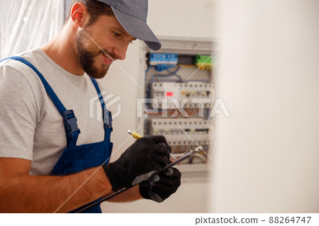 Busy electrical technician writing on a clipboard the data collected on a residential electric panel Busy electrical technician writing on a clipboard the data collected on a residential electric panel 88264747
