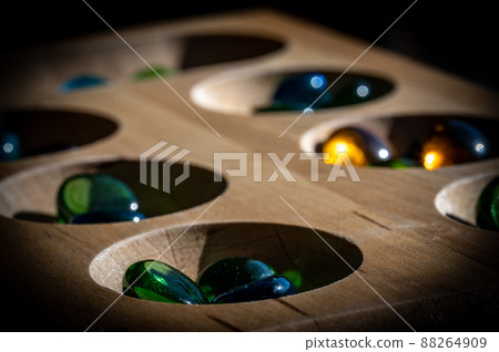 Selective focus on glass beads on a wooden mancala board Selective focus on glass beads on a wooden mancala board 88264909