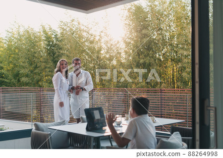 Happy elderly couple resting on the balcony of a luxury house while their son using a tablet. Selective focus 88264998