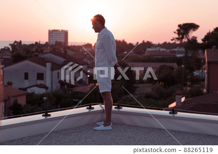 an elderly businessman in casual clothes enjoys the roof of his house at sunset time. Selective focus  88265119