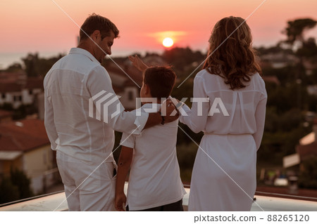 Happy family enjoys and spends time together on the roof of the house while watching the sunset on the open sea together 88265120