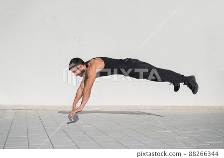 A man in black sportswear jumps while doing push-ups outdoors. A man in black sportswear jumps while doing push-ups outdoors. 88266344
