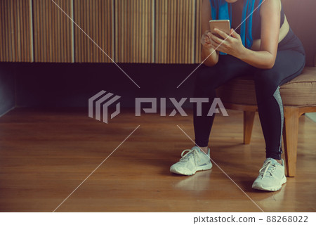 Sportswoman sitting and using smartphone in locker room at gym. Sportswoman sitting and using smartphone in locker room at gym. 88268022