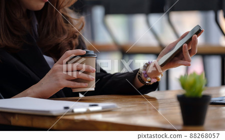 Young Asian woman with smartphone while holding cup of coffee and texting text message on smartphone app. 88268057