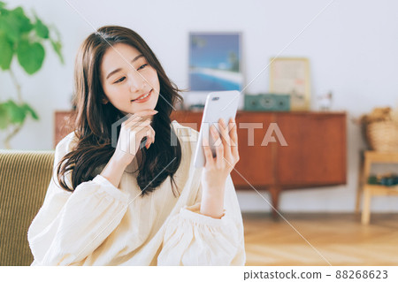 Woman sitting on a sofa and looking at a smartphone Woman sitting on a sofa and looking at a smartphone 88268623