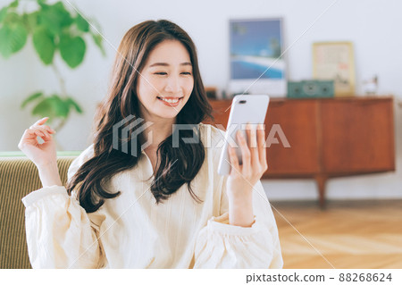 Woman sitting on a sofa and looking at a smartphone 88268624