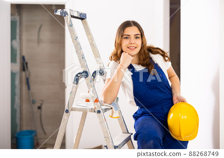 Enthusiastic young female builder in blue overalls and yellow hard hat 88268749