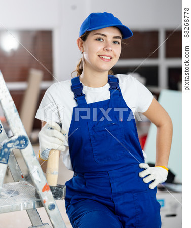 Smiling young female builder in blue uniform at construction site Smiling young female builder in blue uniform at construction site 88268778