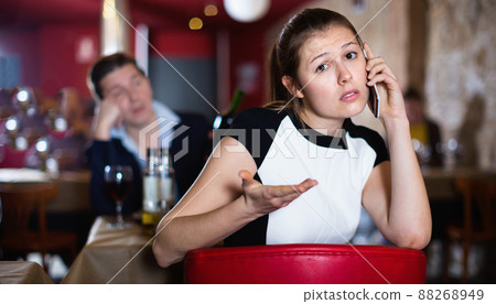 Offended young woman speaking by phone on background with drunk man at restaurant table Offended young woman speaking by phone on background with drunk man at restaurant table 88268949