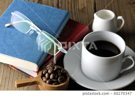 一個帶咖啡豆的勺子、一個帶咖啡的咖啡杯、一個碟子、眼鏡和一本書 一個帶咖啡豆的勺子、一個帶咖啡的咖啡杯、一個碟子、眼鏡和一本書 88270347