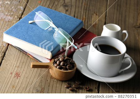 A spoon with coffee beans, a coffee cup with coffee, a saucer, glasses and a book 88270351