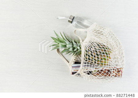 Mesh shopping bag with pineapple, glossy magazine and eco friendly bottle of water on white wooden background. 88271448