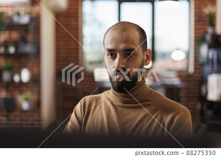 Marketing office employee brainstorming management ideas. Young businessman sitting in office with crossed arms, looking at computer monitor while reviewing financial statistics. 88275350