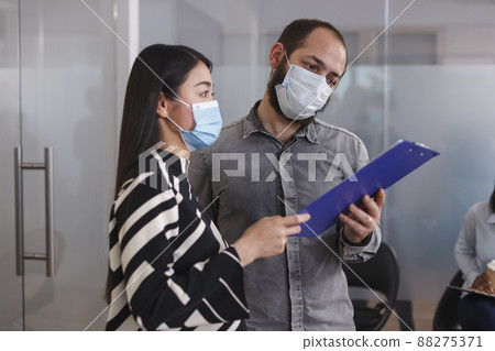HR department manager reviewing job applicant CV resume on clipboard while in lobby area of startup company. Employer and future employee wearing protective mask while standing in waiting room. HR department manager reviewing job applicant CV resume on clipboard while in lobby area of startup company. Employer and future employee wearing protective mask while standing in waiting room. 88275371