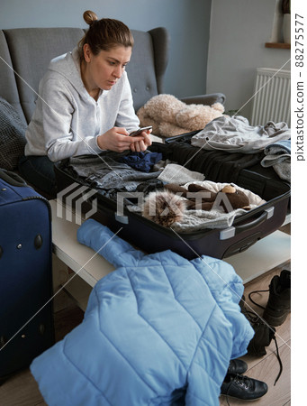 A woman packing things in a suitcase. 88275577