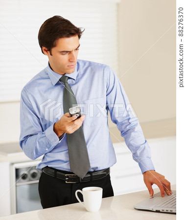 Business executive using cellphone while working on a laptop. Successful young business executive using cellphone while working on a laptop at home. 88276370