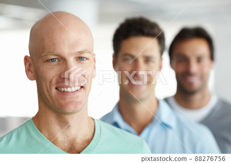 Hes got a great team behind him. Shot of a young man standing in an office with male colleagues in the background. Hes got a great team behind him. Shot of a young man standing in an office with male colleagues in the background. 88276756