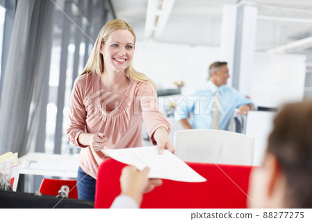 A bright career future is ahead of her. A young female office worker handing a colleague a document with her boss standing in the background. 88277275