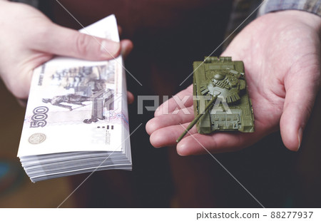 Russian rubles banknotes and toy tank in hands during the war in Ukraine. Inflation, sanctions and the fall of the Russian economy concept. Falling cash savings and budget Russian rubles banknotes and toy tank in hands during the war in Ukraine. Inflation, sanctions and the fall of the Russian economy concept. Falling cash savings and budget 88277937