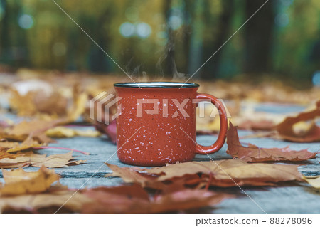Autumn coffee or tea in a cup on a wooden table against the background of yellow fallen leaves and October weather. Autumn drink, mood and comfort concept. Autumn coffee or tea in a cup on a wooden table against the background of yellow fallen leaves and October weather. Autumn drink, mood and comfort concept. 88278096