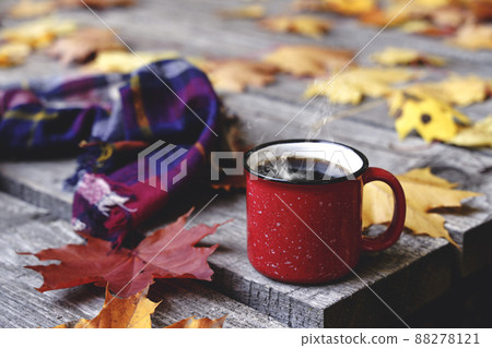 Autumn coffee or tea in a cup on a wooden table against the background of yellow fallen leaves and October weather. Autumn drink, mood and comfort concept. Autumn coffee or tea in a cup on a wooden table against the background of yellow fallen leaves and October weather. Autumn drink, mood and comfort concept. 88278121