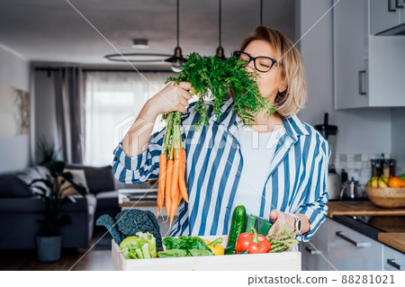 Woman checking fresh organic carrots from a wooden box with fresh vegetables. Local farmer healthy food. New Start of a healthy life, weight loss concept. Online home food delivery. Copy space. 88281021