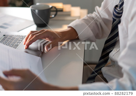 Overwork Concept The office personnel in the loose tie sitting at his desk, reading a paperwork and typing on the notebook Overwork Concept The office personnel in the loose tie sitting at his desk, reading a paperwork and typing on the notebook 88282179