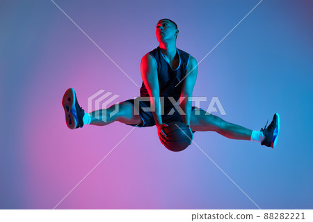Young sportive man playing basketball isolated on blue studio background in neon light. Youth, hobby, motion, activity, sport concepts. 88282221