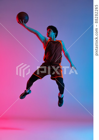 Young energetic man playing basketball isolated on gradient pink blue studio background in neon light. Youth, hobby, motion, activity, sport concepts. 88282265