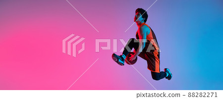 Young energetic man playing basketball isolated on gradient pink blue studio background in neon light. Youth, hobby, motion, activity, sport concepts. 88282271