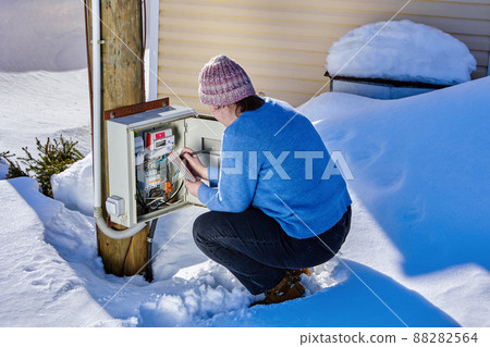 Woman takes readings from external electric meter outside in winter. 88282564
