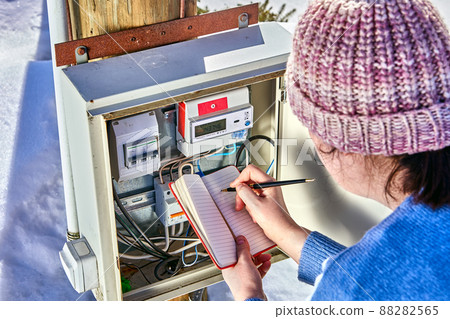 Woman readings from external electric meter outdoors. 88282565