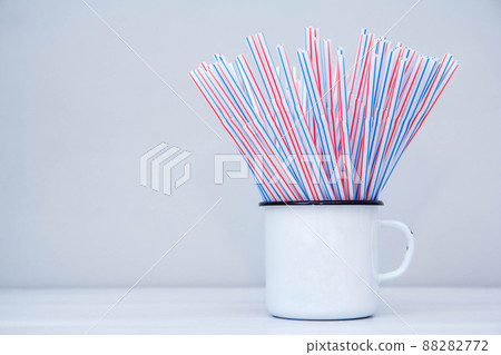 Drinking plastic straws in white metal mug on a gray background. Colorful of plastic straws used for drinking water or soft drinks. Copy space Drinking plastic straws in white metal mug on a gray background. Colorful of plastic straws used for drinking water or soft drinks. Copy space 88282772