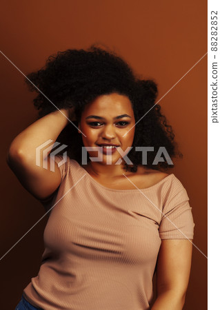 pretty young african american woman with curly hair posing cheerful gesturing on brown background, lifestyle people concept 88282852