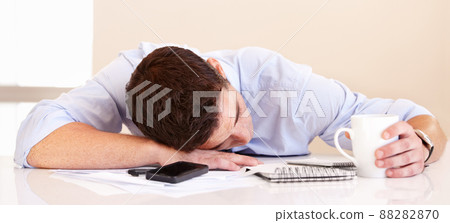 Hes got no energy left. Exhausted businessman lying on his desk along with his mobile phone. 88282870