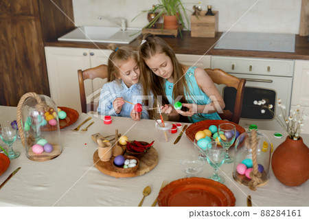 Two sweets sisters are busy coloring Easter eggs in the kitchen. The festive tradition of Easter. Coloring eggs in bright colors. Preparing for a religious holiday Two sweets sisters are busy coloring Easter eggs in the kitchen. The festive tradition of Easter. Coloring eggs in bright colors. Preparing for a religious holiday 88284161