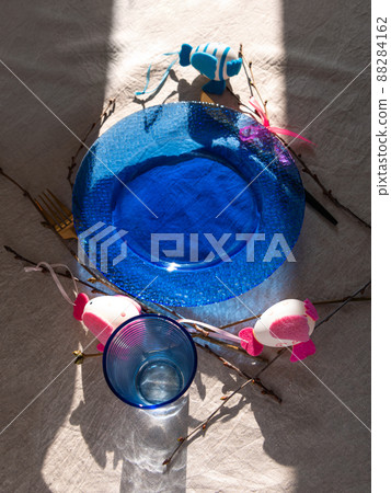Easter table setting empty blue glass plate cutlery tree branches linen cloth flat lay harsh shadow Festive dish place Easter table setting empty blue glass plate cutlery tree branches linen cloth flat lay harsh shadow Festive dish place 88284162