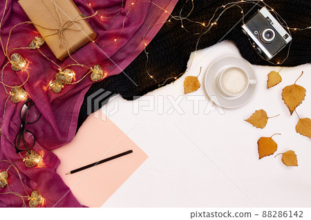 Romantic autumn mock up. Sheet of pink paper, yellow and orange leaves, pencils, cup of cappuccino and old camera.Top view. Flat lay. 88286142