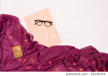 Black glasses, pink paper with new years goals. Scarf and Christmas lights on white background. Black glasses, pink paper with new years goals. Scarf and Christmas lights on white background. 88286164